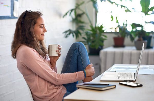 Female remote staff with a coffee mug working from home in laptop